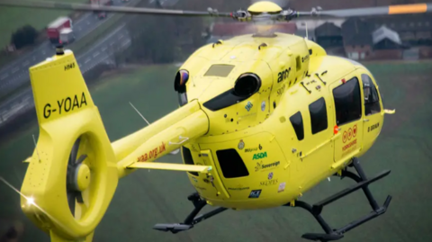 A yellow Yorkshire Air Ambulance in flight. 