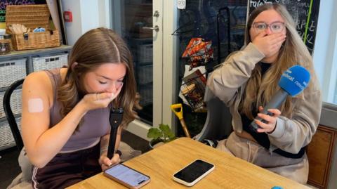 Two stunned girls react to their exam results with their hands over their mouths in shock