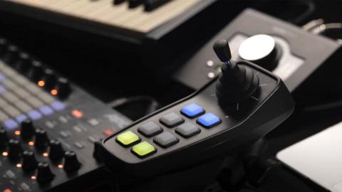 Image of a 'composer' device which is a joystick with 8 buttons. The 'composer' is resting on top of a mixing desk.