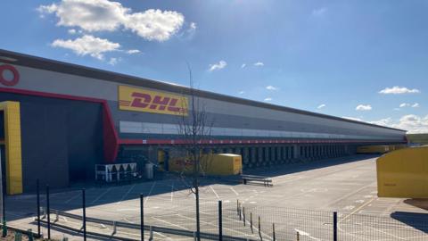 A red "DHL" sign on the side of a yellow van. 