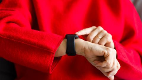 Close-up shot of a person in a bright red sweater, using a smart watch on their wrist
