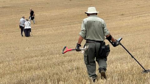 A group of metal detectorists in a field on a bright sunny day.