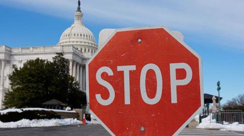 A stop sign is visible amid patches of snow in front of the US Capitol Building in Washington, DC