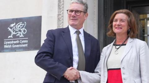 A smiling Sir Keir Starmer and Eluned Morgan shake hands on the steps of the Welsh government building in Cathays Park, Cardiff