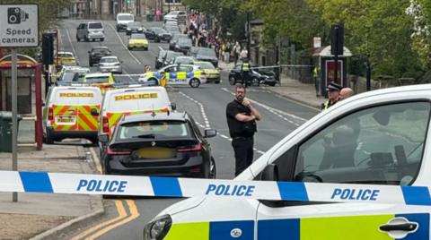 A road with multiple police cars parked and a police cordon. 
