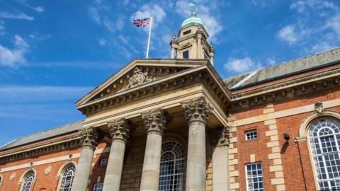 Front of Peterborough Town Hall, a red-brick building with four columns by the entrance and a union flag flying on the top