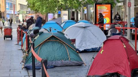 A row of different coloured tents behind barriers on a busy shopping street in Liverpool.