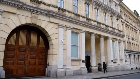 The front of Bristol Crown Court with archway and stone pillars by the entrance to the building. There is a pedestrian walking along the pavement in front of the building. 