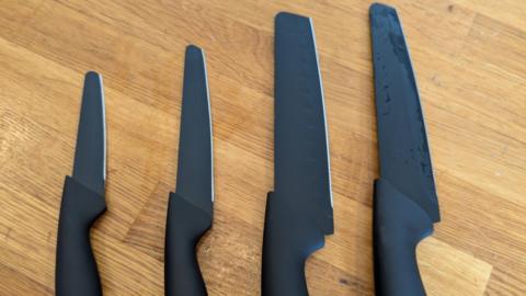 Four rounded-tip charcoal grey kitchen knives of varying size laid out on a wooden table.