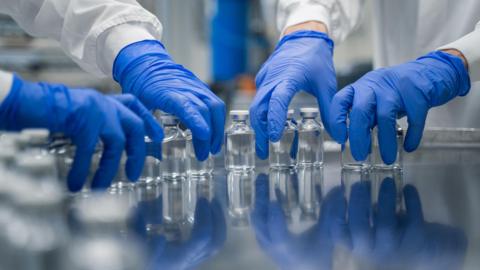 Blue gloved hands in a lab picking up vials of clear liquid