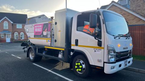 A small white bin lorry on a road in a residential area.
