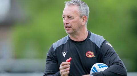 Former Catalans Dragons head coach Steve McNamara holding a rugby league ball and a whistle