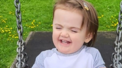 Eleanor who has brown hair with a clip in it, on a swing with her eyes closed, laughing