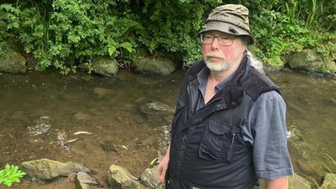 Man standing next to river with dead fish.