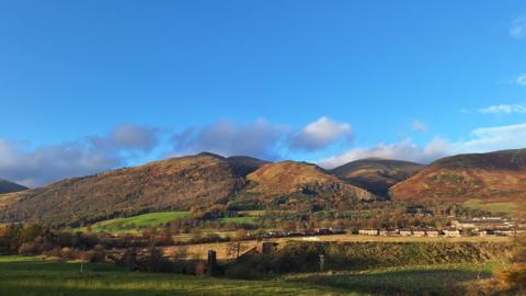 Blue skies and light cloud over an autumnal mountain scene