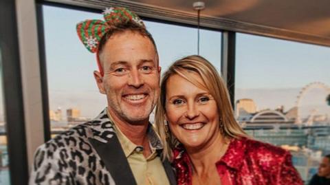 A middle-aged couple smile in fancy dress. 