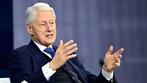 Bill Clinton is seen sitting and emoting with his hands as he speaks