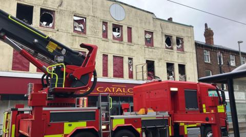 A close up of a fire engine in front of the empty former three-storey Ex Catalogue Outlet building on Lord Street, Fleetwood, taken the morning after a fire. Most of its windows are damaged by the fire.