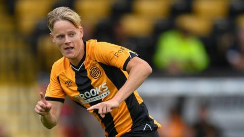 Cambridge United midfieler George Hoddles runs and points in home kit