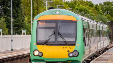 A Southern Railways train in its green, yellow and white livery, pulls up at a rural station. There are no passengers.
