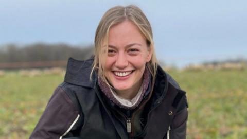 Hannah Murrell a shepherdess who is crouched down in a field with her sheepdog Roo.