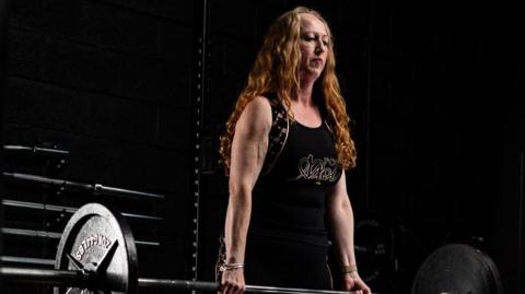 Jane Bennett lifting a weight in a dark gym.