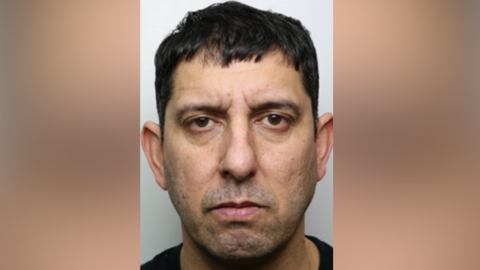 Abdullah Shahnamy is pictured wearing a black t-shirt in a police mugshot. 