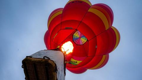 A hot air balloon, rising from the ground with the burner on full