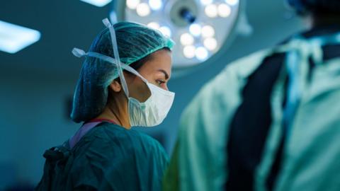 A masked female surgeon in an operating theatre