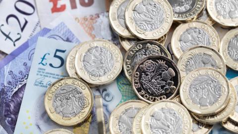 Pound coins on top of bank notes which include a £5 and £20 note. 