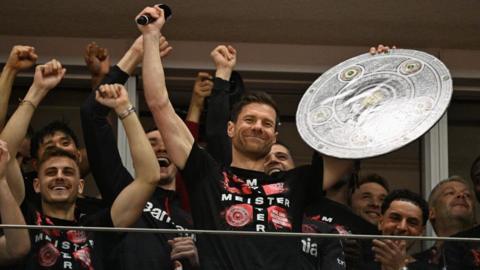 Bayer Leverkusen boss Xabi Alonso celebrates with a mock-up of the Bundesliga trophy with his players