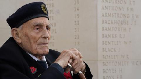 Royal Navy D-Day veteran John Dennett, 101, at the British Normandy Memorial in Ver-sur-Mer, France, ahead of a Service of Remembrance to mark the 81st anniversary of the D-Day landings. He is dressed in a black suit, white shirt and black tie. He is wearing a red poppy and is and holding a wooden cane.