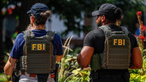File image of the back of two FBI agents, wearing bullet-proof vests with the writing 'FBI' in yellow