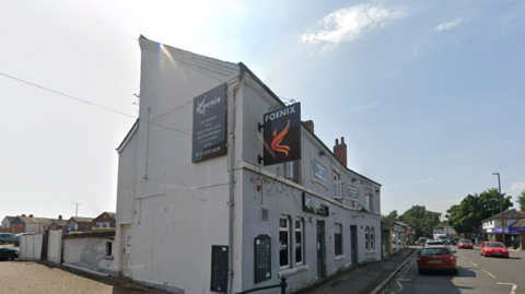 A sign which reads Foenix on the side of a white building with a red car to the right