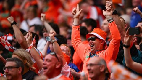 Group of people in the orange of Armagh cheering with their arms raised in a crowd