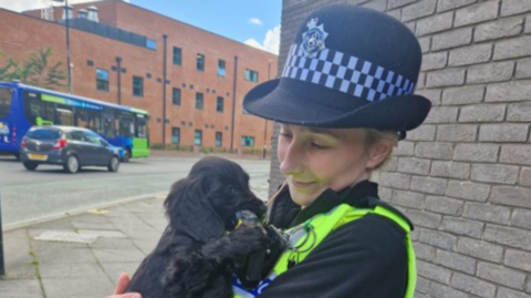 Police officer holding a black Cocker Spaniel puppy