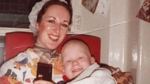 Antonya Cooper is pictured cuddling her son Hamish in old family photo. Hamish has lost his hair from cancer treatment. They are sitting on what appears to be a hospital armchair. Antonya is wearing a small hat and a flowery top. Hamish is wrapped in a blanket and both are smiling.