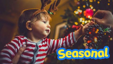 Child wearing reindeer antlers and dressing a Christmas tree. 