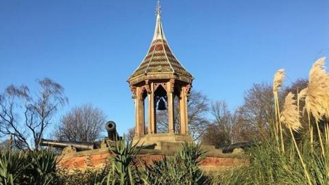 A spired oriental-style tower surrounded by cannons and greenery 