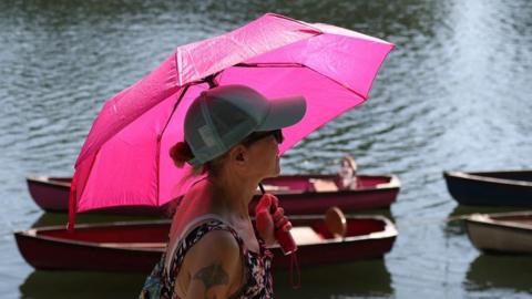 A person uses an umbrella to shield from the sun whilst walking along the River Thames, as Britain experiences record temperatures disrupting schools and transport networks, at Richmond, in London, Britain, June 25, 2026