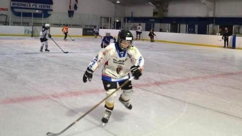 Ice hockey players skate across the ice rink inside the centre. The players are wearing helmets and padding.