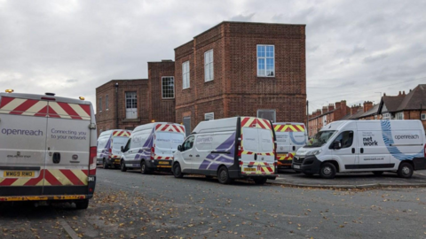 Multiple white vans with broadband company branding parked outside a brick building near Trent Bridge, Nottingham