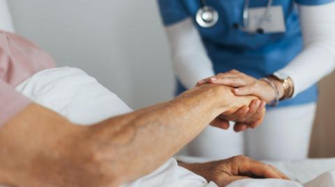 Stock image of a hospital patient in bed, holding a doctor's hand.