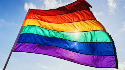 Pride flag flying in a blue sky