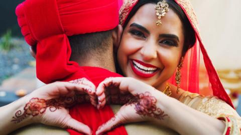 Shot of a happy young woman hugging her husband and making a heart gesture on their wedding day.