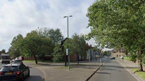 A Google maps image showing a road junction with cars to the left and buildings in the distance