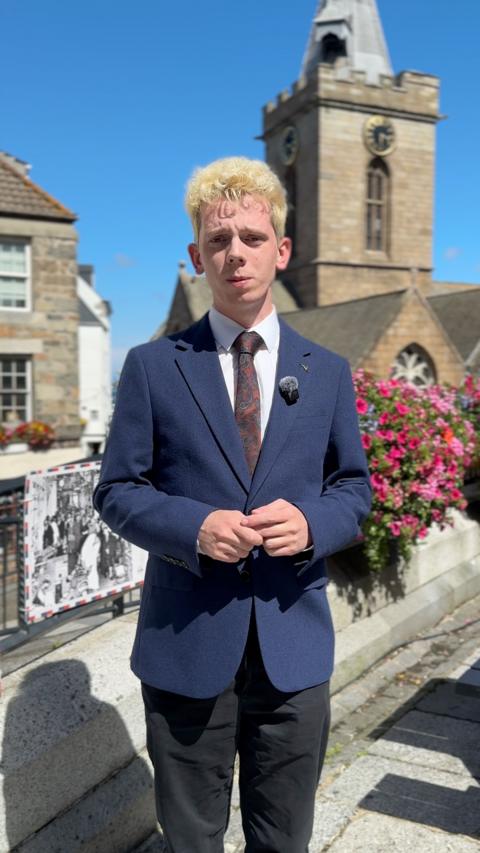 A man with blonde hair wearing a blue suit looking at the camera