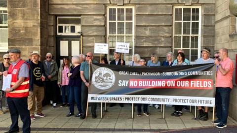 A dozen people gather outside the civic centre in Stoke holding large banners that read 'say no building on our fields'.