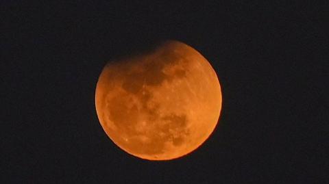 A partial lunar eclipse taking place on an orange-hued Moon