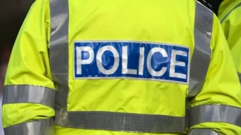 The back of a police hi-vis jacket. It has grey strips and a blue rectangle to the centre with the word 'Police' written in white.